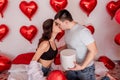 Loving couple kissing while sitting on bed decorated with heart shaped balloons. Valentines Day Royalty Free Stock Photo