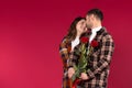 A loving couple with flowers on a red background look cute into each other`s eyes. Empty side space Royalty Free Stock Photo