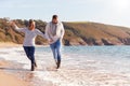 Loving Couple Holding Hands As They Walk Along Shoreline Of Beach Through Waves Royalty Free Stock Photo