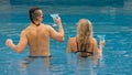 The loving couple hugs and kisses, drinking blue cocktail alcohol liquor in swimming pool at hotel outdoor. Portrait of Royalty Free Stock Photo