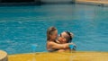 The loving couple hugs and kisses, drinking blue cocktail alcohol liquor in swimming pool at hotel outdoor. Portrait of Royalty Free Stock Photo