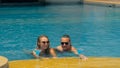 The loving couple hugs and kisses, drinking blue cocktail alcohol liquor in swimming pool at hotel outdoor. Portrait of Royalty Free Stock Photo