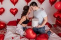 Loving couple kissing while sitting on bed decorated with heart shaped balloons. Valentines Day Royalty Free Stock Photo