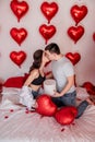 Loving couple kissing while sitting on bed decorated with heart shaped balloons. Valentines Day Royalty Free Stock Photo