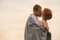 Loving couple kissing in sunset engulfed in a blanket for warmth
