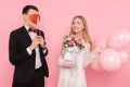 A loving couple, a man holding two paper hearts in his eyes, and a woman holding a bouquet of flowers, on a pink background Royalty Free Stock Photo