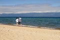 A loving couple of a man and a woman walks along the sand coastline of Lake Baikal on a mountain background on a sunny day. Royalty Free Stock Photo