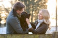 Loving Couple With Pet Spaniel Dog Leaning On Fence On Snowy Walk In Winter Countryside