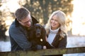 Loving Couple With Pet Spaniel Dog Leaning On Fence On Snowy Walk In Winter Countryside