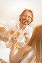 Loving couple raising wineglasses of champagne having event at beach cafe. Selective focus on laughing man against the Royalty Free Stock Photo