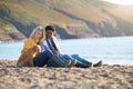 Loving Couple Sitting On Sand As They Walk With Dog Along Shoreline On Winter Beach Vacation Royalty Free Stock Photo