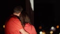 A loving couple stands hugging at the window at night, back view