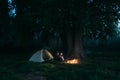 loving couple of travelers in the woods sitting by the fire near the tent. Tourists guy and girl are resting at night Royalty Free Stock Photo