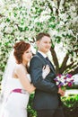 Loving couple under blossoming branches spring day. Young adult brunette man and woman kissing in fresh blossom apple