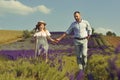 A loving couple is walking along the lavender field, a girl in a dress and a straw hat with a man holds hands and walks through