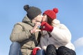 Loving couple in winter hats kissing against the blue sky and keeps hands in heart shape sign