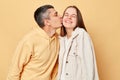 Loving couple woman and man wearing casual style clothing standing isolated over beige background expressing love, husband kissing