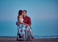 Loving couple, a woman sits on her husband`s lap, resting on a beach against a background of a bright dawn.