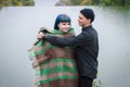 Loving couple wrapped in plaid sitting on mountain outdoors on sunset. River view. Man and woman traveling together. Royalty Free Stock Photo