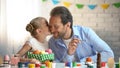 Loving daughter kissing father on cheek, painting eggs for Easter festival
