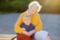 Loving elderly grandmother tenderly embracing his joyful little grandson during walking at summer park. Mother`s day holiday