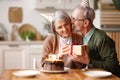 Loving elderly man congratulating woman wife, giving present and kissing gently in cheek