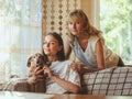 Loving elderly mother hug adult 20s daughter from behind while daughter sitting on couch and holding their dog. looking at camera Royalty Free Stock Photo