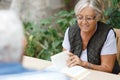 Loving elderly spouses resting in garden and enjoying days, sitting outdoors.Woman reading book, man in front of her Royalty Free Stock Photo