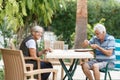 Loving elderly spouses resting in garden and enjoying days, sitting outdoors.Woman reading book, man in front of her Royalty Free Stock Photo