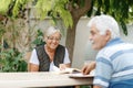 Loving elderly spouses resting in garden and enjoying days, sitting outdoors.Woman reading book, man in front of her Royalty Free Stock Photo