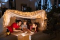 Loving family, mother, father and daughter lying inside self-made hut, tent in room in the evening and reading book Royalty Free Stock Photo