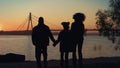 Loving family silhouette walking to river shore together at beautiful sunset. Royalty Free Stock Photo