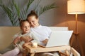 Loving family spending time together. Cute mother with daughter looking at laptop on sofa at home hugging enjoying good time Royalty Free Stock Photo