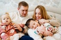 a loving family with two playful children lies in a cozy bed in the home bedroom