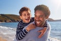 Loving Father Giving Son Piggyback As They Walk Along Winter Beach Together