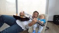 An attractive father plays guitar to his adorable baby boy in a baby swing Royalty Free Stock Photo