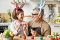 Loving grandfather and child in bunny ear headbands decorating eggs for Easter in light cozy kitchen