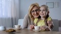 Loving grandma drinking tea with cute granddaughter, tightly hugging her, family Royalty Free Stock Photo