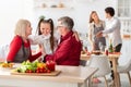 Loving grandparents hugging their cute granddaughter while cooking festive dinner at home