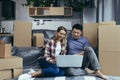 Loving and happy couple sitting on the floor, Asian man and woman among cardboard boxes, looking at laptop screen, shopping online Royalty Free Stock Photo