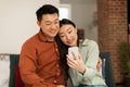 Loving happy korean spouses video calling via cellphone, middle aged man and his young wife relaxing on sofa at home Royalty Free Stock Photo