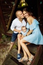 Parents hugging with little daughter. Loving husband gentle kiss beautiful wife, sitting on the stairs outdoors, parents Royalty Free Stock Photo