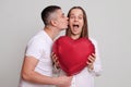 Loving husband kissing amazed excited wife on Valentines Day celebrating together Caucasian man and woman holding heart shaped air Royalty Free Stock Photo