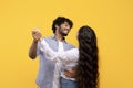 Loving indian couple holding hands and dancing, hugging and smiling at each other while having date, yellow background