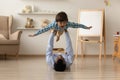 Loving Indian father lifting excited son pretending flying on floor