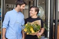 Loving Male Gay Couple Holding Hands Coming Out Of Florists Holding Bunch Of Flowers