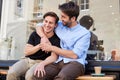 Loving Male Gay Couple Sitting Outside Coffee Shop Hugging