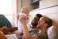 Loving Male Same Sex Couple Cuddling Baby Daughter In Bedroom At Home Together Royalty Free Stock Photo