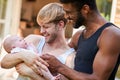 Loving Male Same Sex Couple Cuddling Baby Daughter At Home In Garden Together