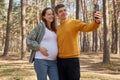 Loving man and pregnant woman walking in park hugging couple making selfie in spring forest husband holding smartphone capturing Royalty Free Stock Photo